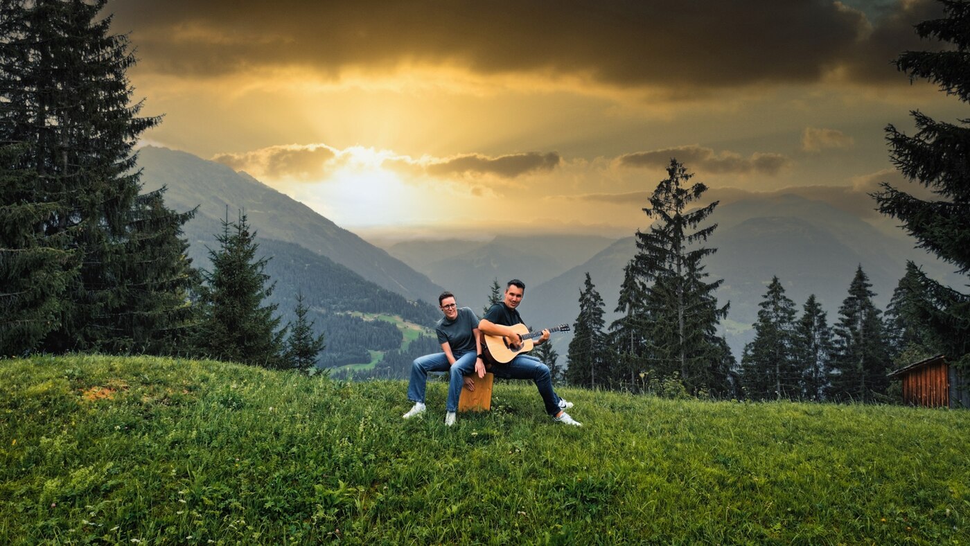 Samuel und Karo musizieren vor der Bergkulisse des Montafons bei Sonnenuntergang