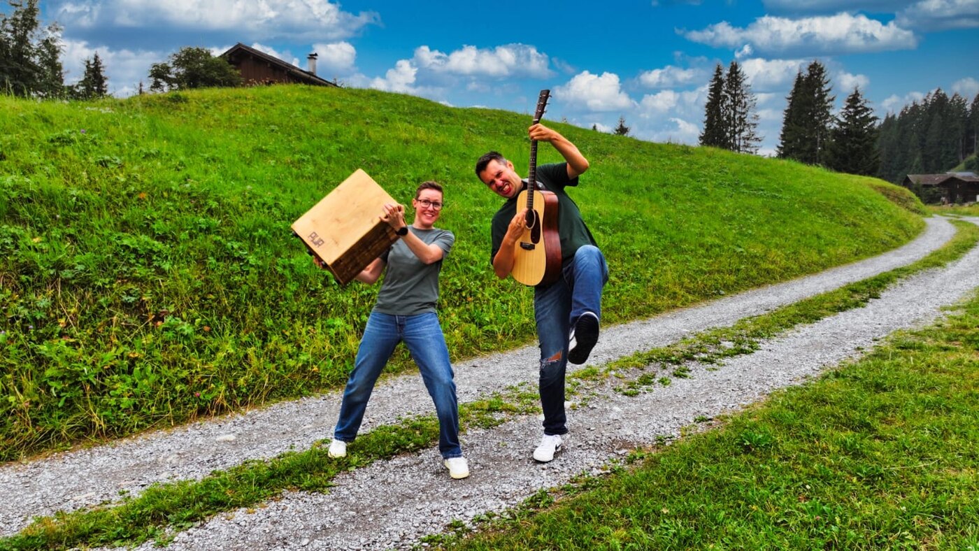 Samuel und Karo mit Gitarre und Cajon auf einer Wiese im Montafon