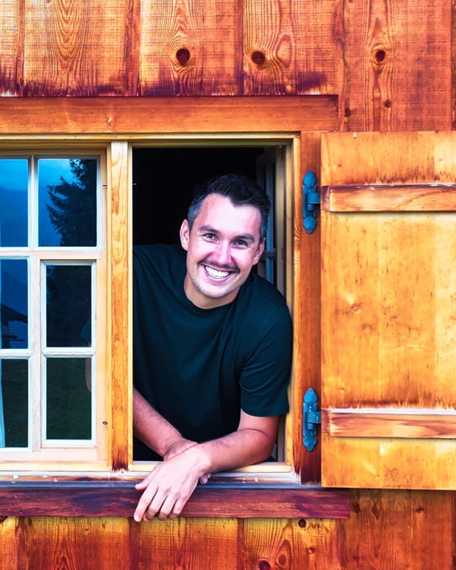 Samuel von The Timbertones lehnt lachend aus dem Fenster einer Holzhütte
