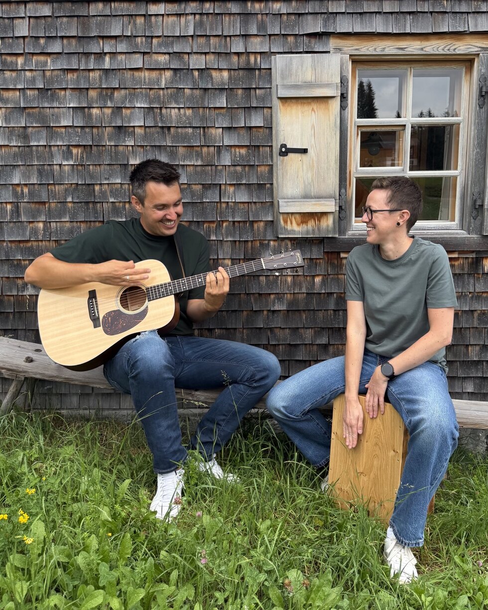 Samuel mit Gitarre und Karo am Cajon vor einer Montafoner Holzhütte